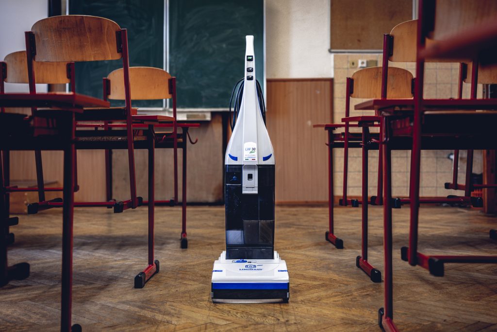 Podlahový umývací stroj LINDHAUS LW30 postavený na drevenej podlahe školskej triedy vedľa stolov so stoličkami pred tabuľou