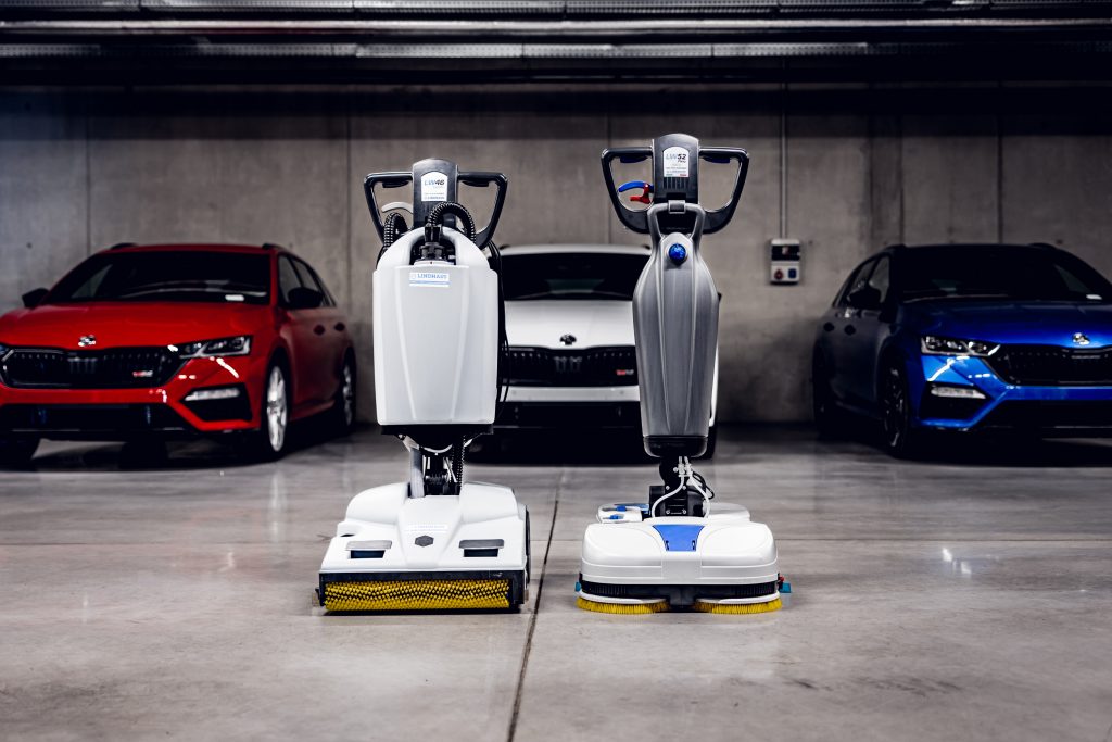 Podlahové umývacie stroje LINDHAUS LW46 a LW52 Flexy na betónovej podlahe garáže autosalóna s autami v pozadí